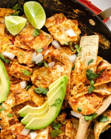 A featured image of chilaquiles rojos in a black skillet close up to see the toppings.