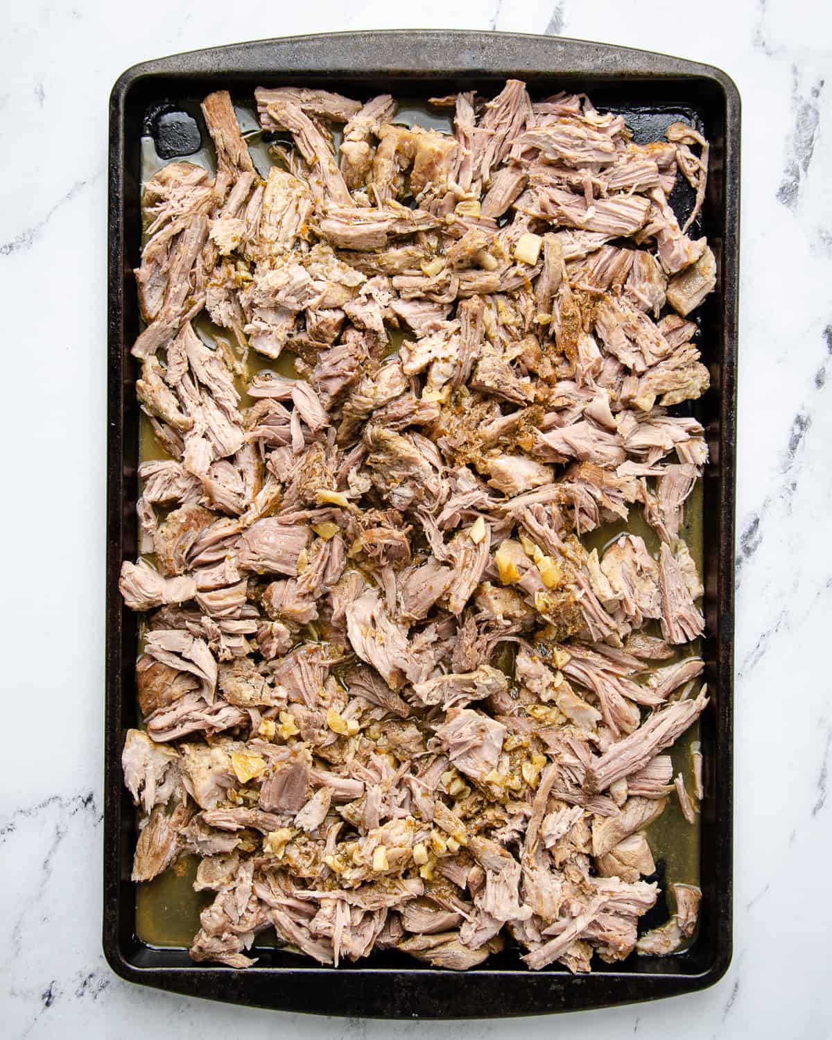 The shredded carnitas on a sheet tray covered in the cooking sauce.