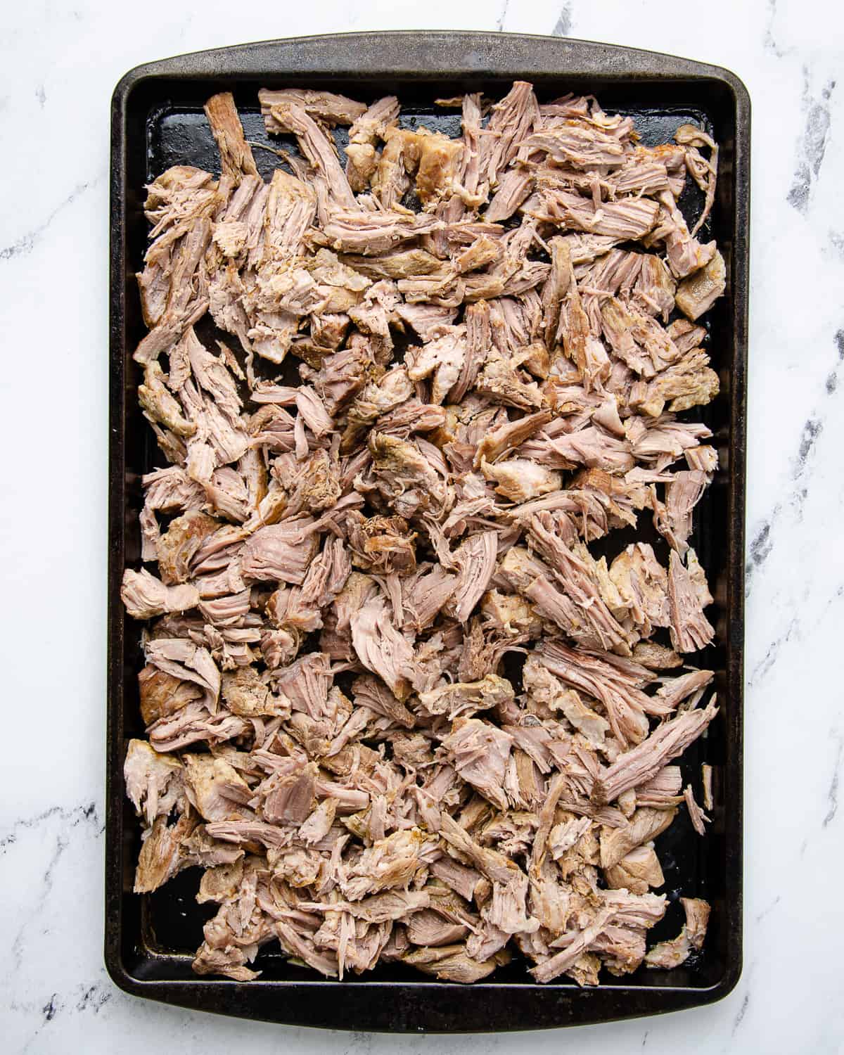 Shredded pork carnitas on a sheet tray ready to be broiled.