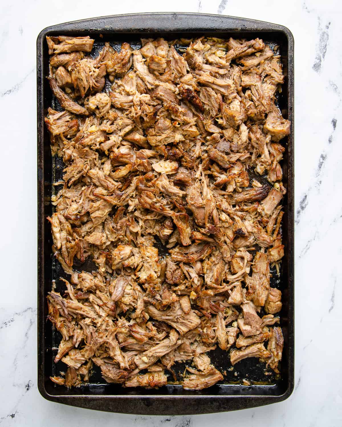 Broiled and browned shredded pork carnitas on a sheet tray.