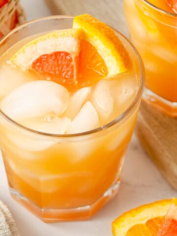 A glass of grapefruit orange juice with orange slices in it.
