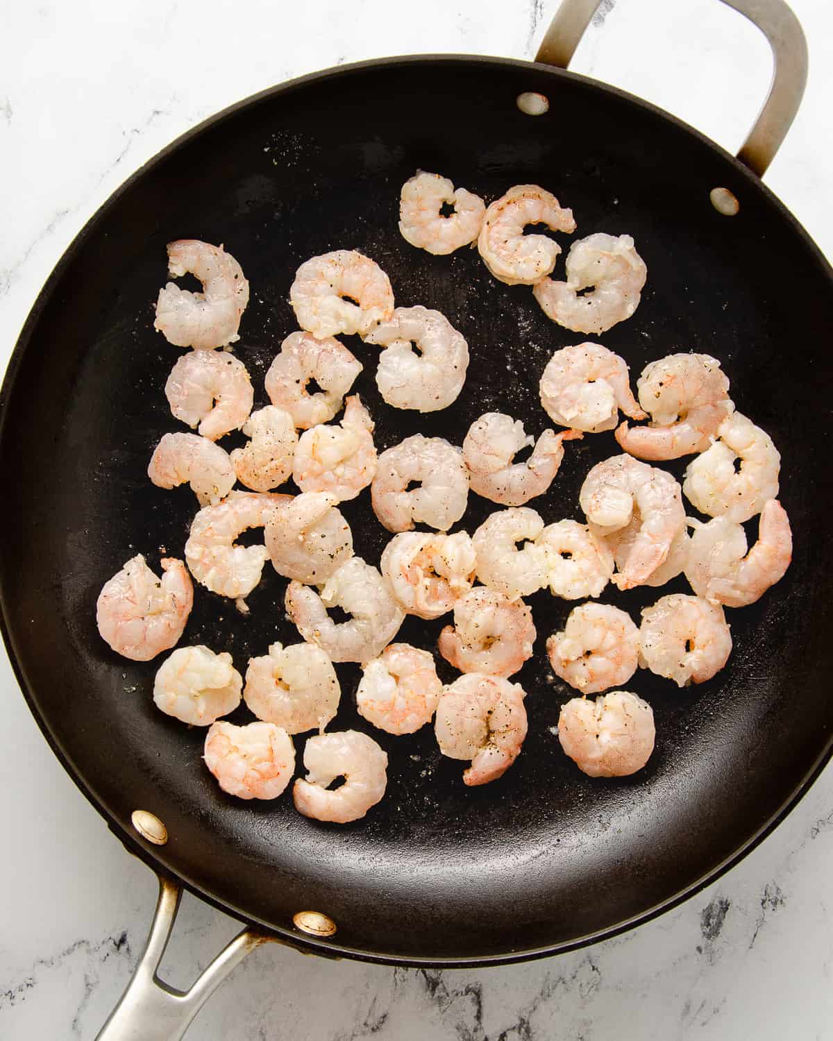 A skillet with cooking seasoned shrimp.