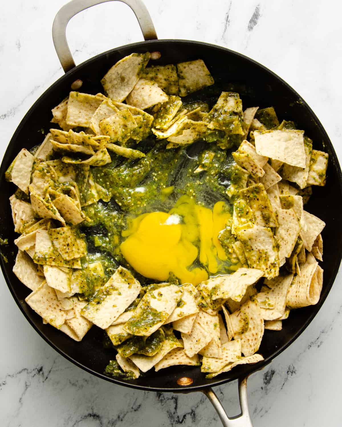 A skillet with tortilla chips, salsa verde, and eggs.