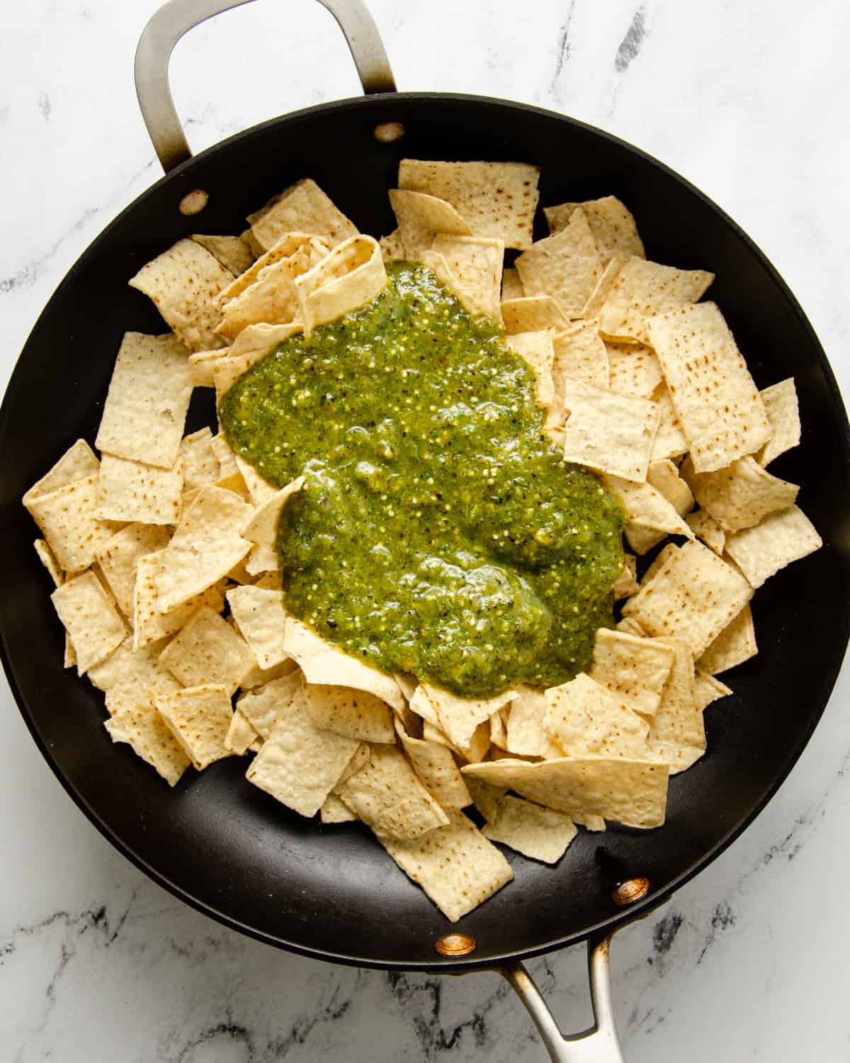 A skillet with tortilla chips and salsa verde.