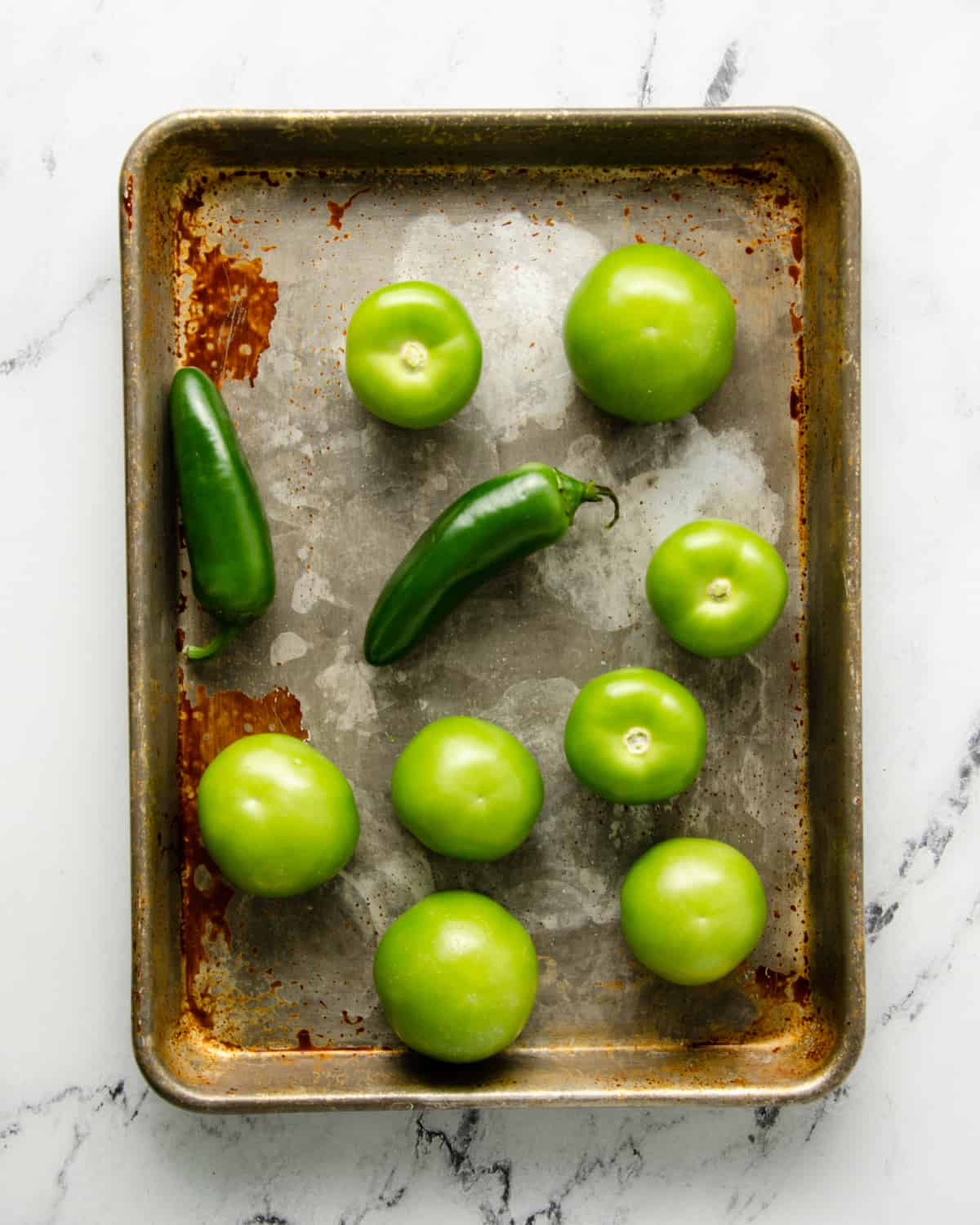 Tomatillos and peppers on a baking sheet before roasting.