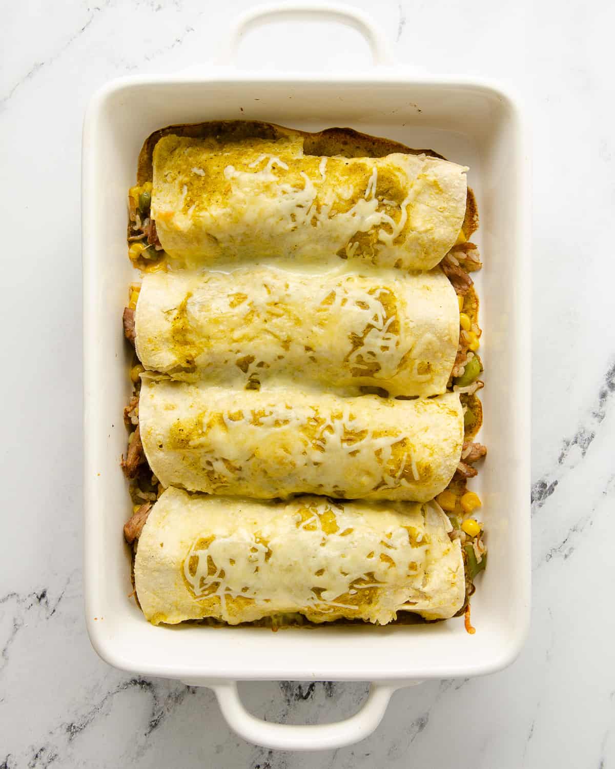 Baked carnitas enchiladas topped with sauce and cheese after baking.