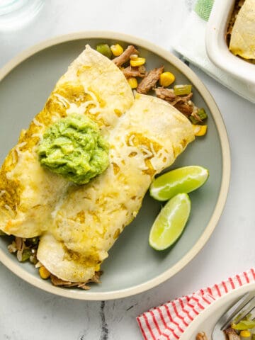Two enchiladas on a plate topped with cheese and a scoop of guacamole.