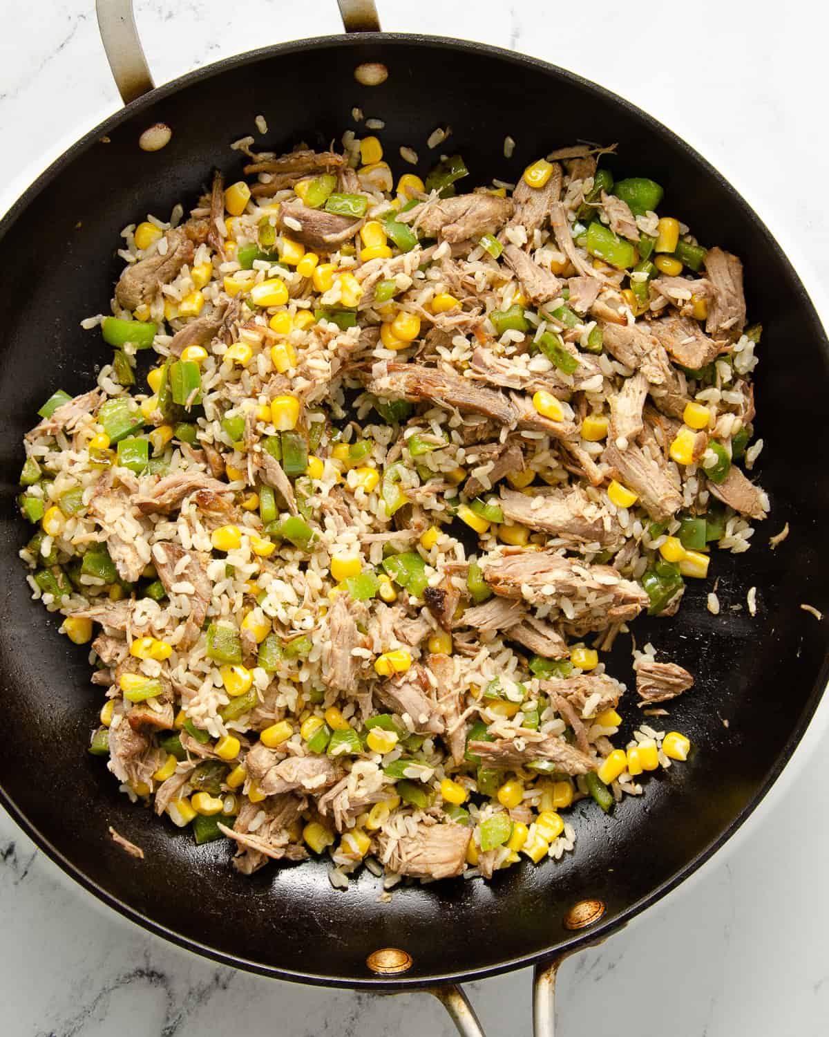 Carnitas, rice, peppers, and corn in a skillet.