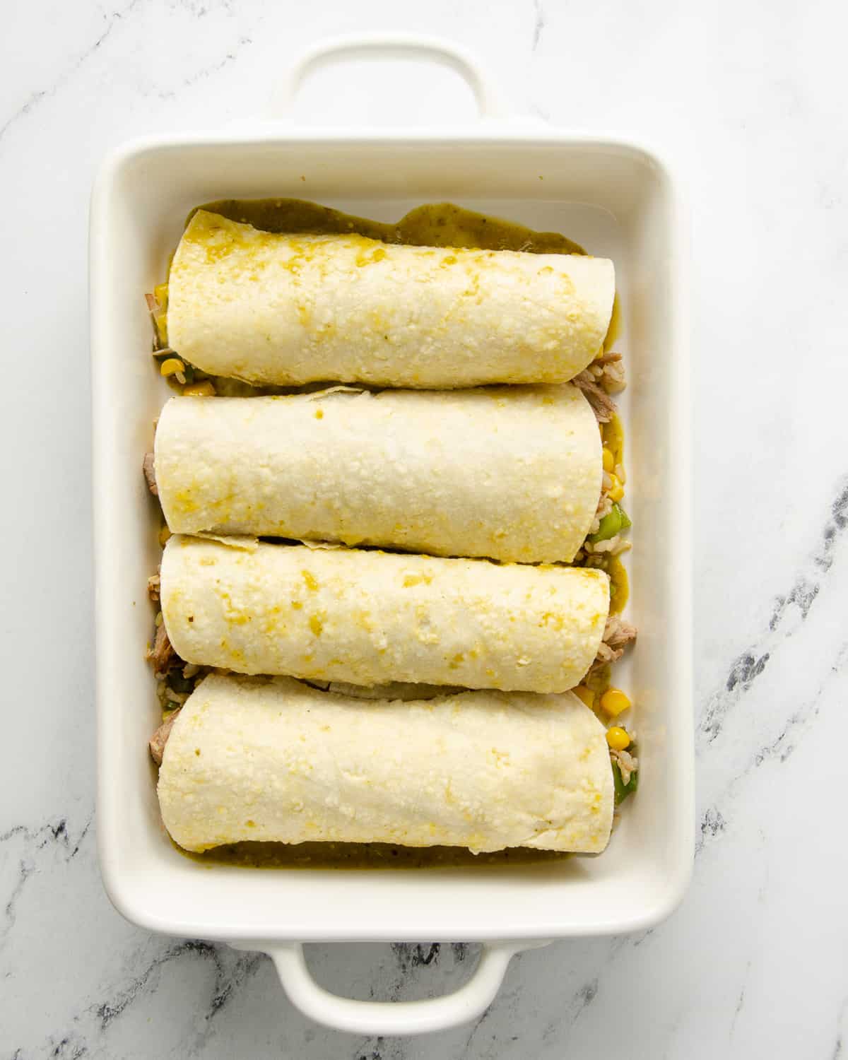 Enchiladas rolled up in a white baking dish before baking.
