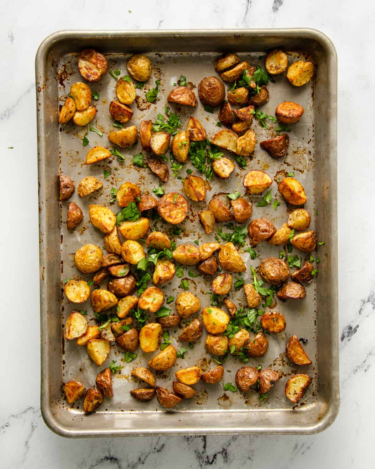 Roasted potatoes on a baking sheet with fresh cilantro.