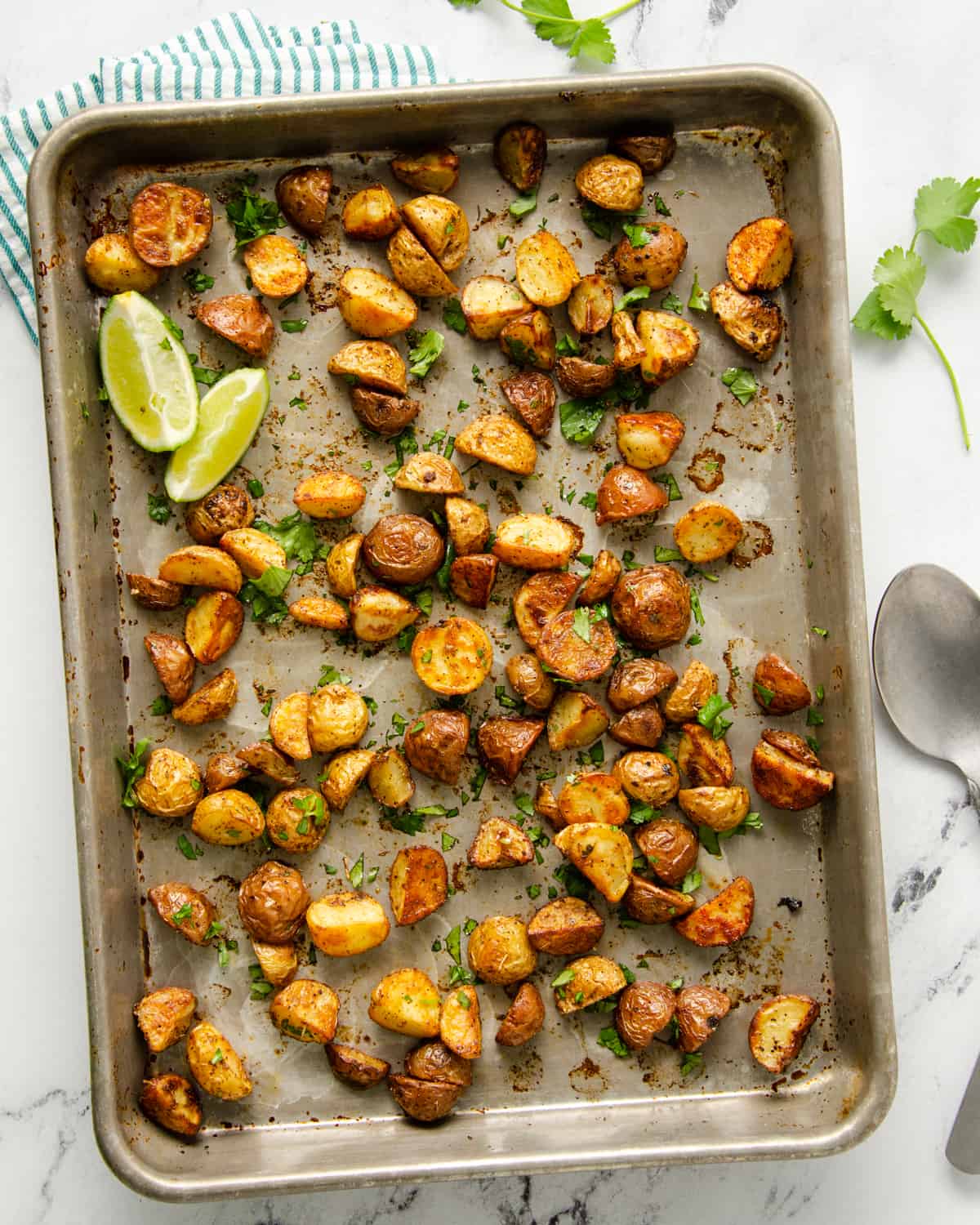 Roasted Mexican breakfast potatoes on a baking sheet with lime wedges and topped with cilantro.