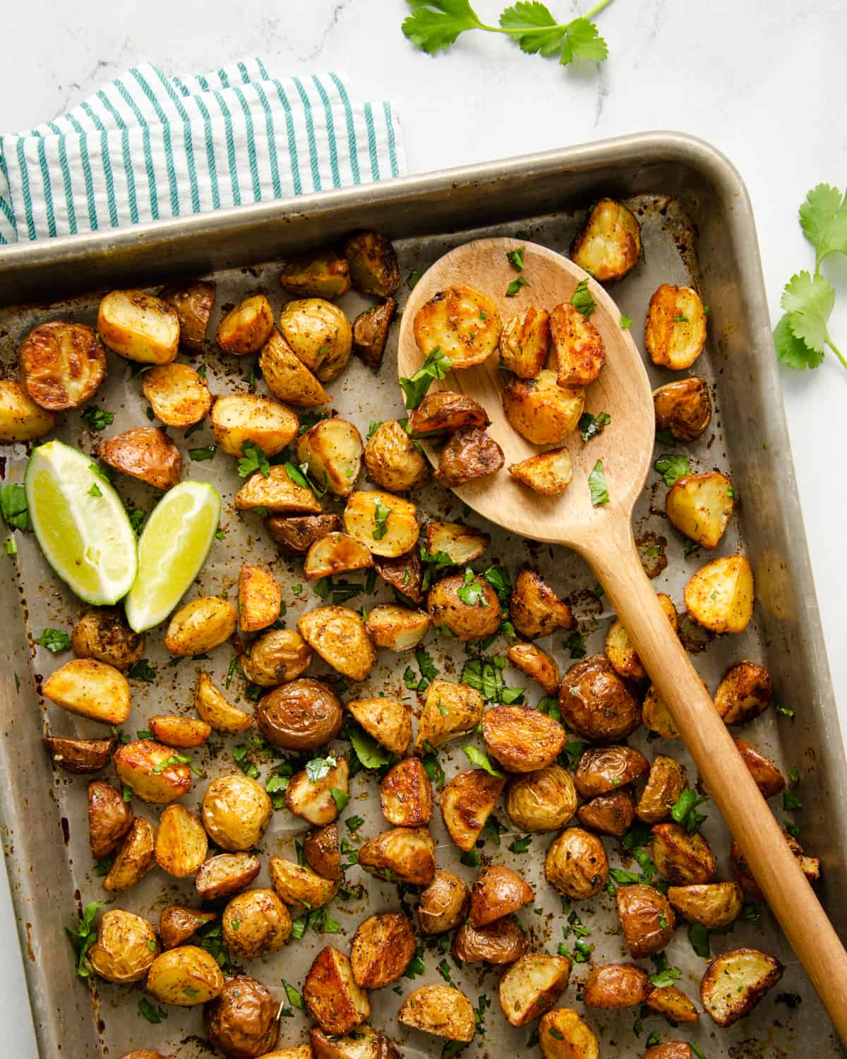 Roasted Mexican breakfast potatoes on a baking sheet with lime wedges and topped with cilantro.
