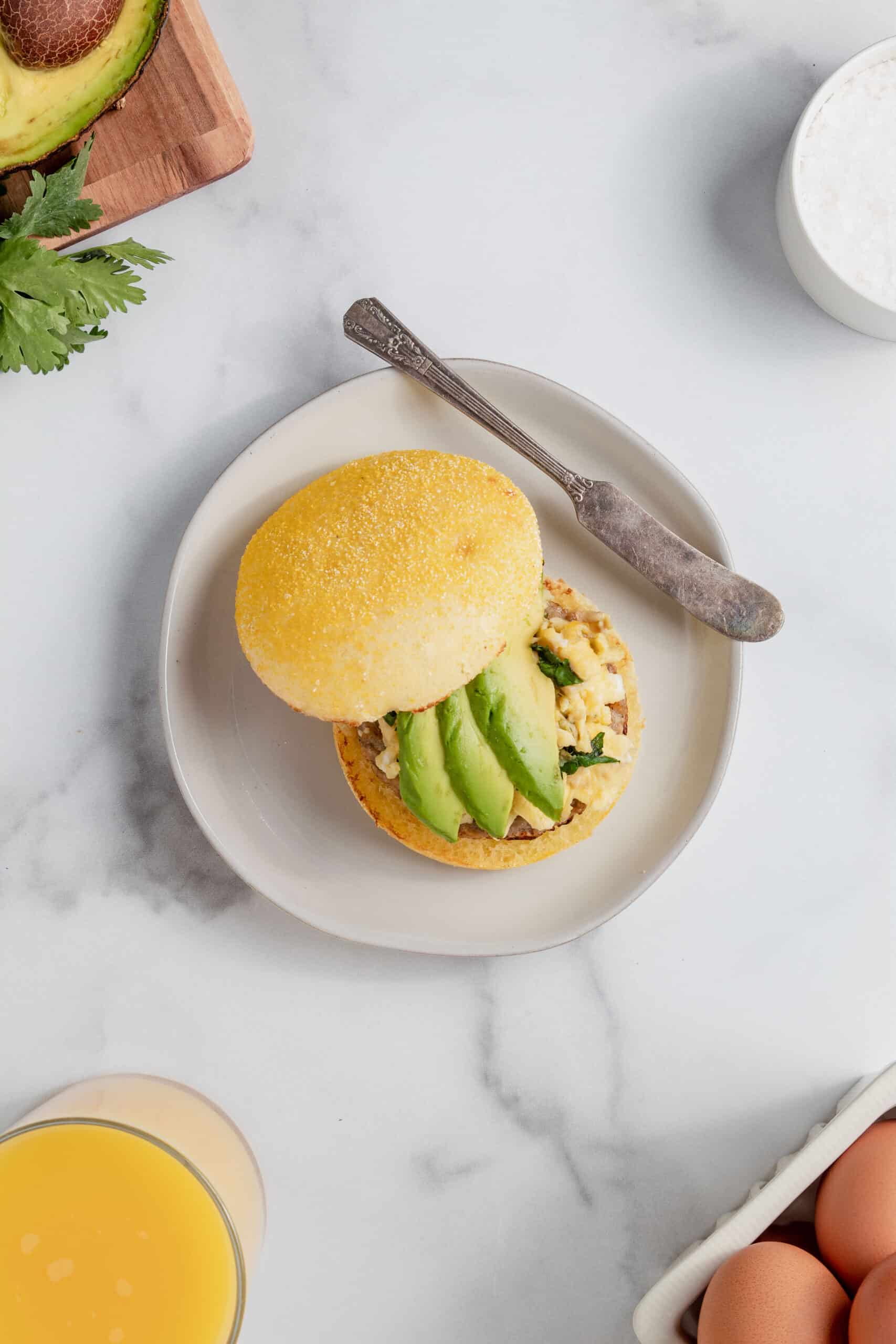 Breakfast sandwich with eggs and avocado on a white plate.