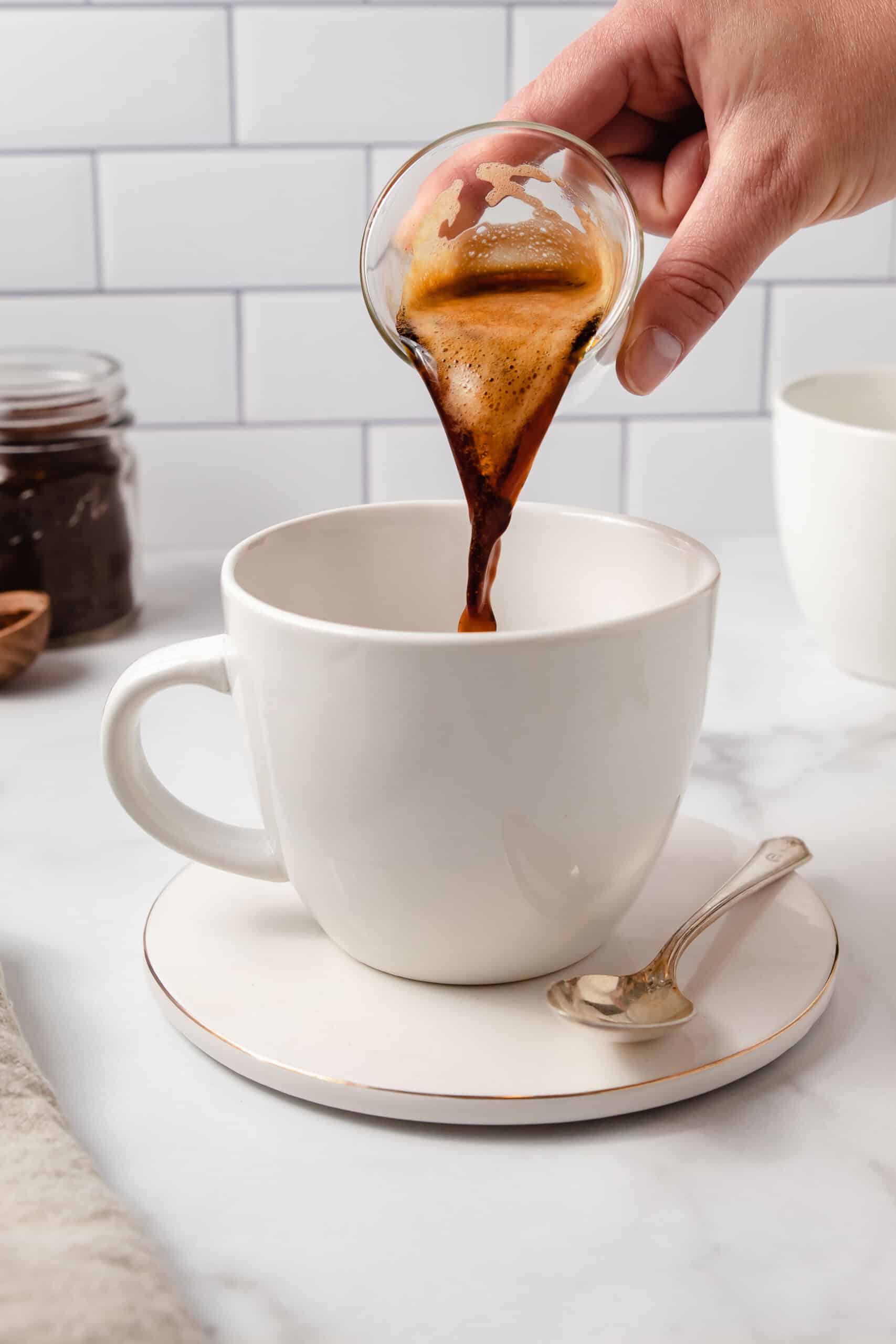 Pouring an espresso shot into a white latte mug.