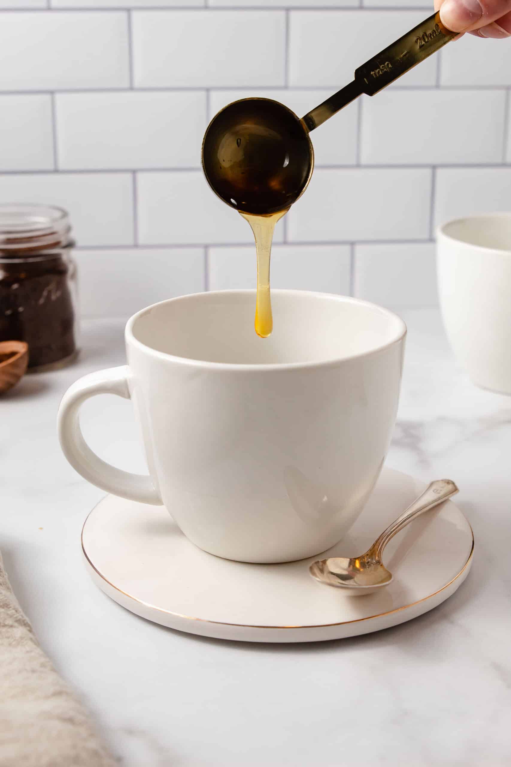 A hand dripping honey into a coffee mug.