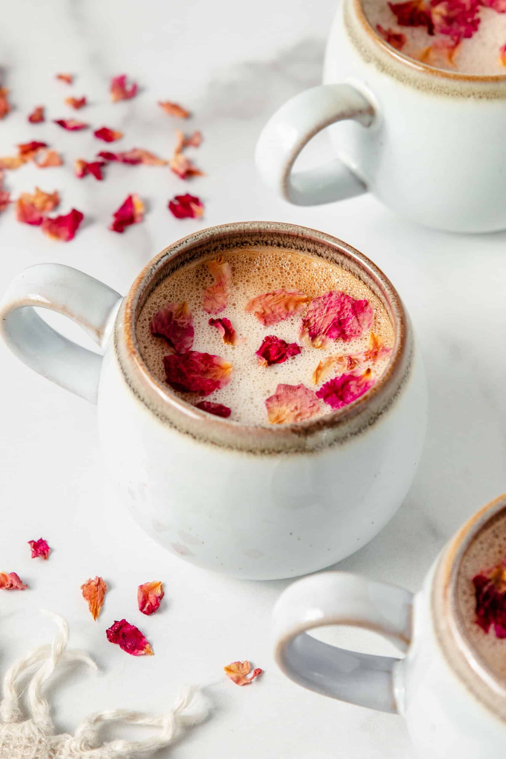 Rose latte with rose petals in a white coffee mug.