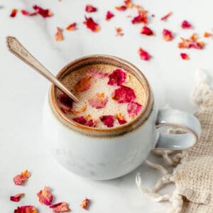 Rose latte with rose petals in a white coffee mug with a spoon.