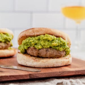 Breakfast burger on an english muffin topped with guacamole on a cutting board.