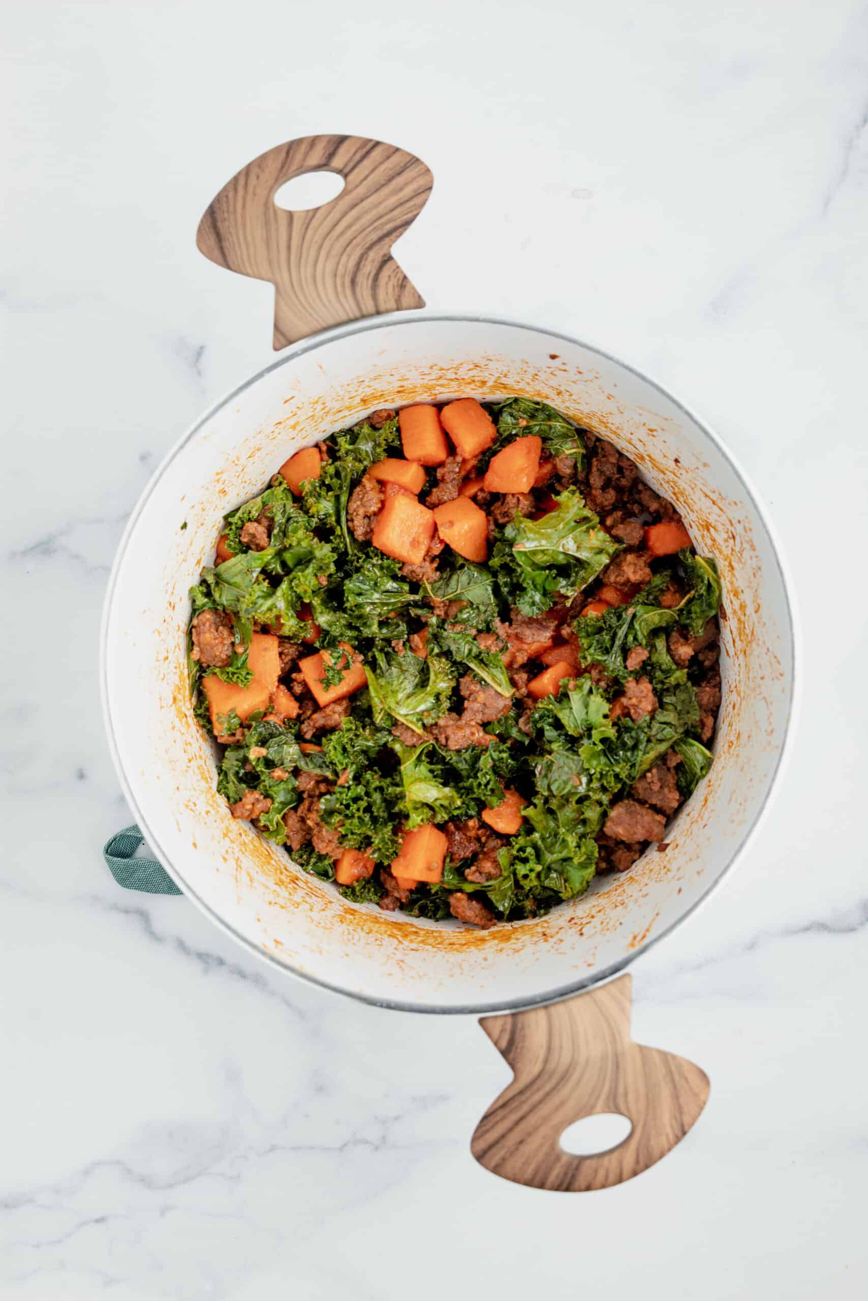 Kale, sweet potatoes, and chorizo topped with enchilada sauce in a pot.