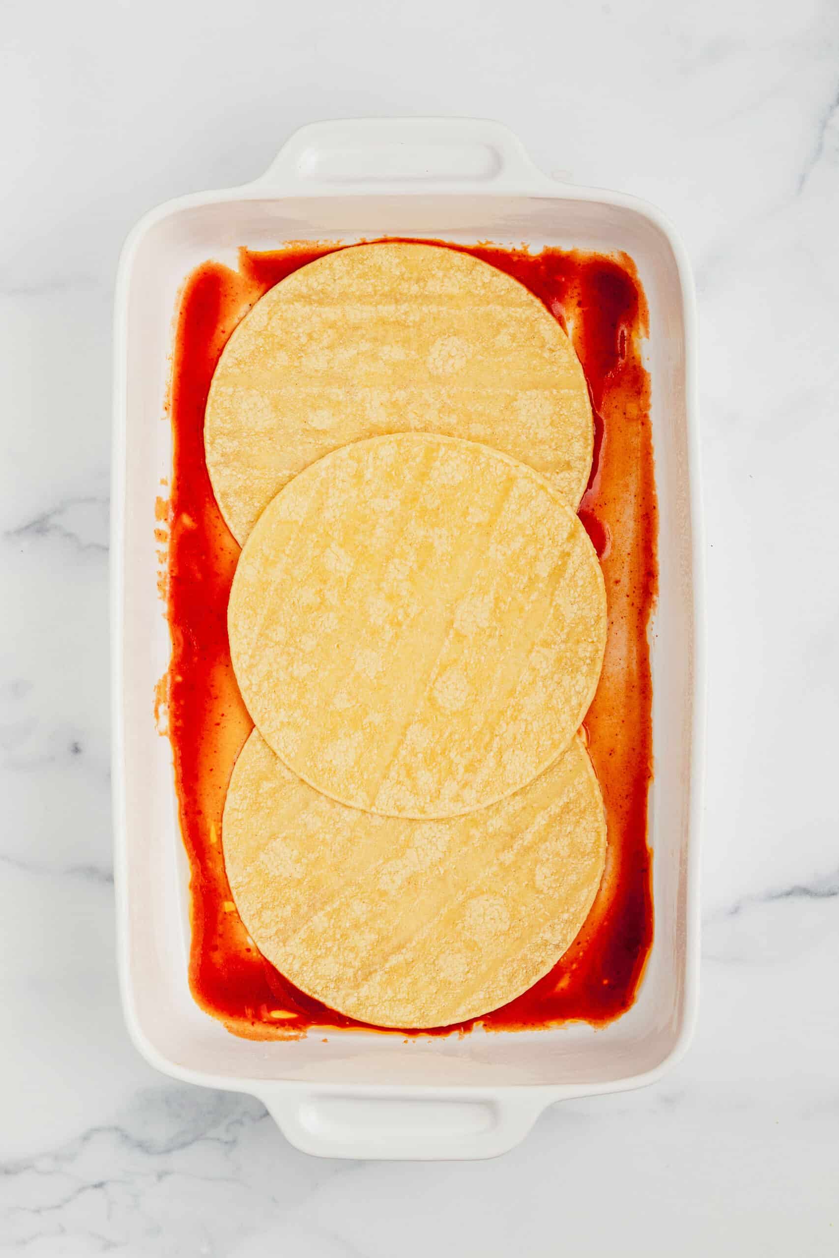 Enchilada sauce with tortillas in a casserole dish.