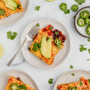 A slice of gluten free enchilada casserole topped with cilantro, limes, and avocado.