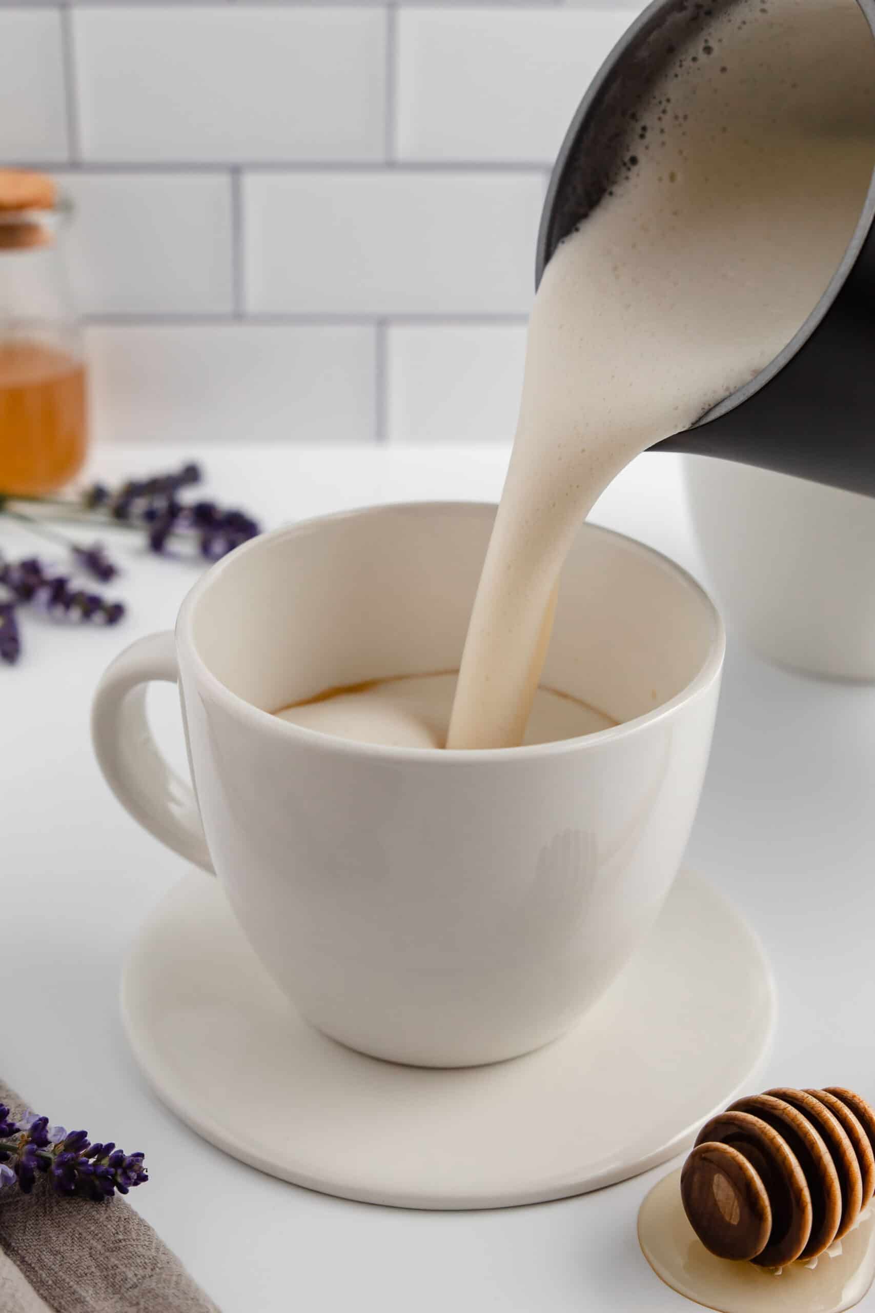 Pouring frothed milk into a white coffee mug.