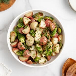 A white bowl with potatoes and Brussels sprouts tossed with mustard dill dressing.
