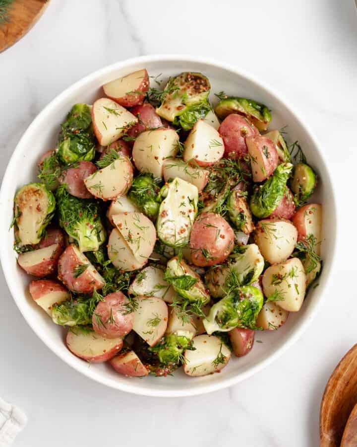 A white bowl with potatoes and Brussels sprouts tossed with mustard dill dressing.