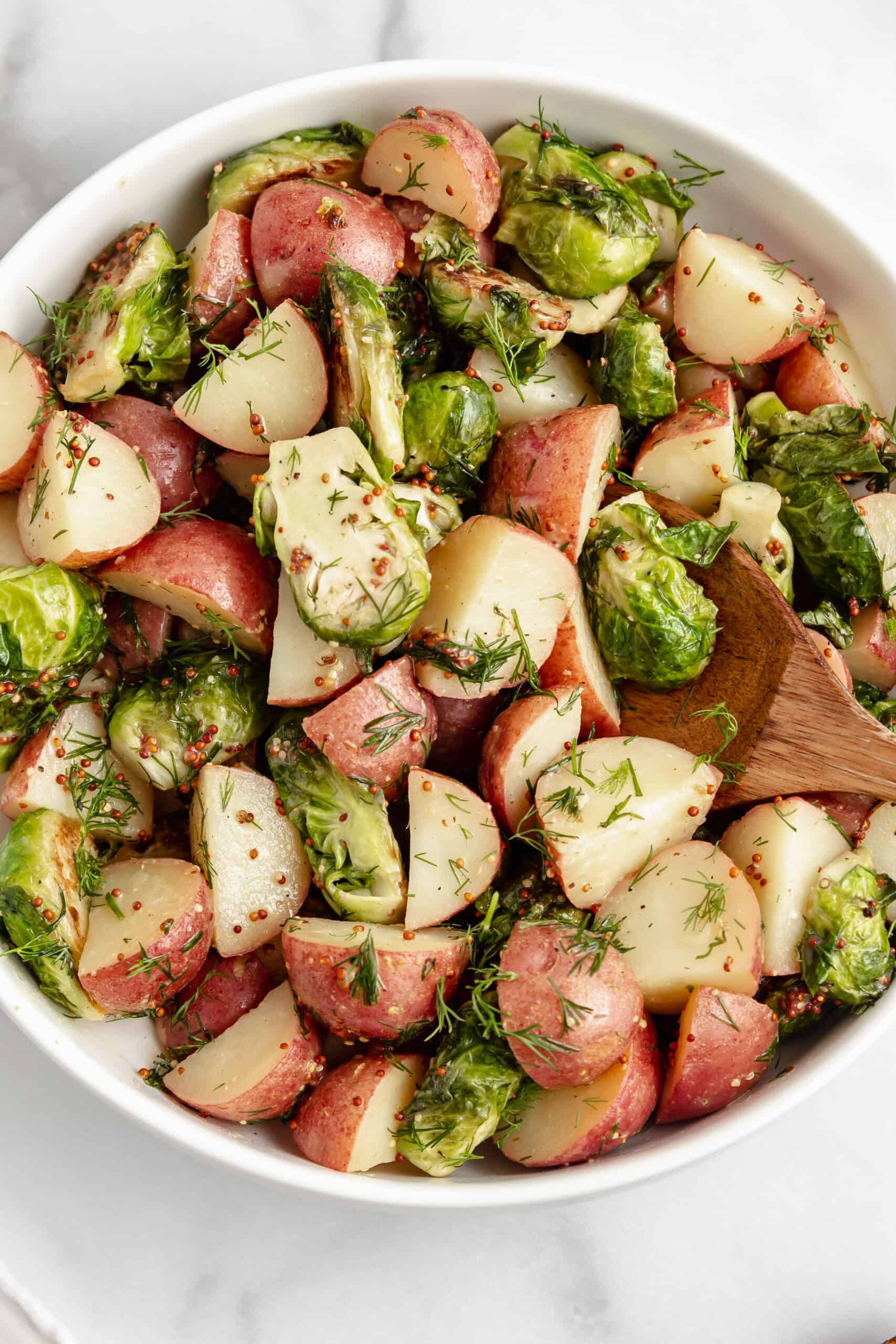 Up close bowl with potatoes and Brussels sprouts tossed with mustard dill dressing.