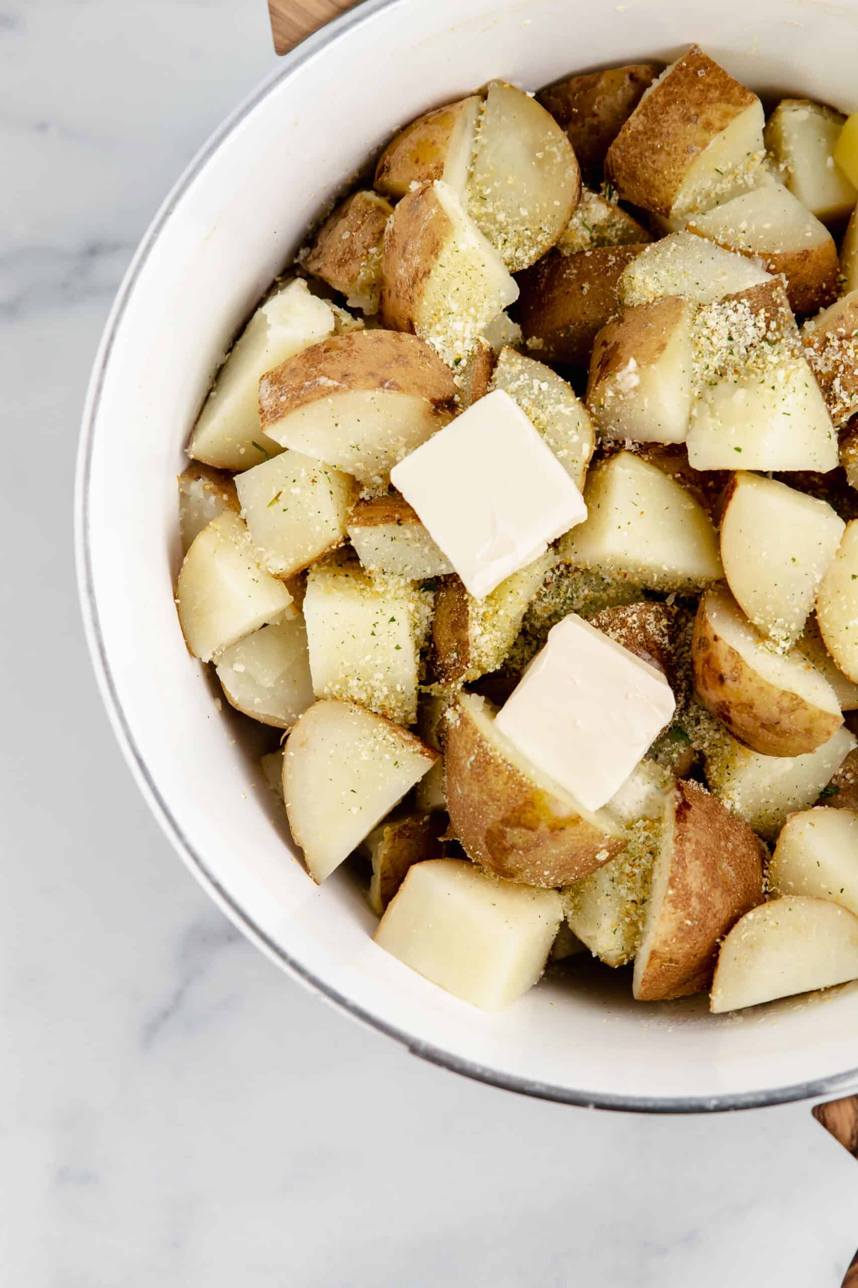 A bowl of diced potatoes with garlic salt and butter.