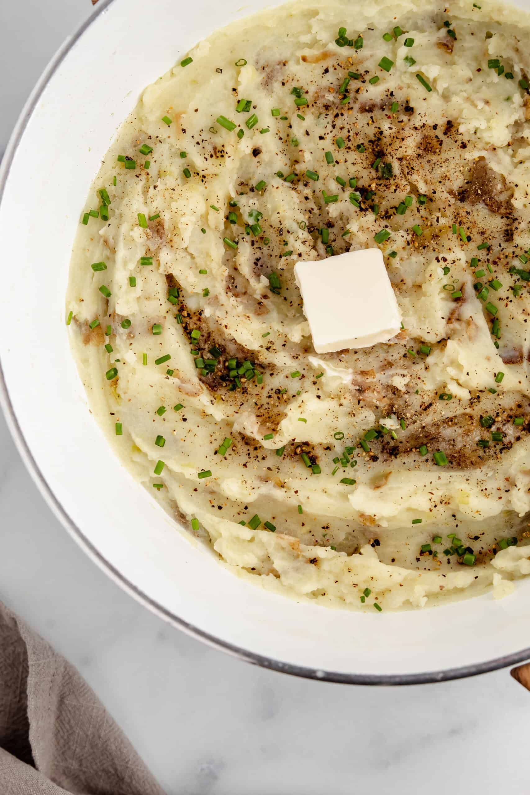 A bowl of mashed potatoes topped with salt, pepper, butter, and chives.