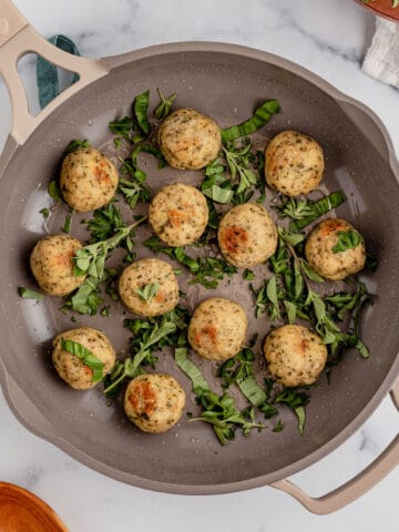 Chicken meatballs in a skillet with fresh herbs.