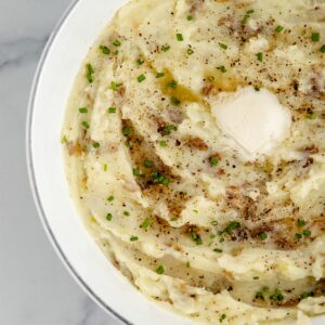 Featured image of A bowl of mashed potatoes topped with salt, pepper, butter, and chives.
