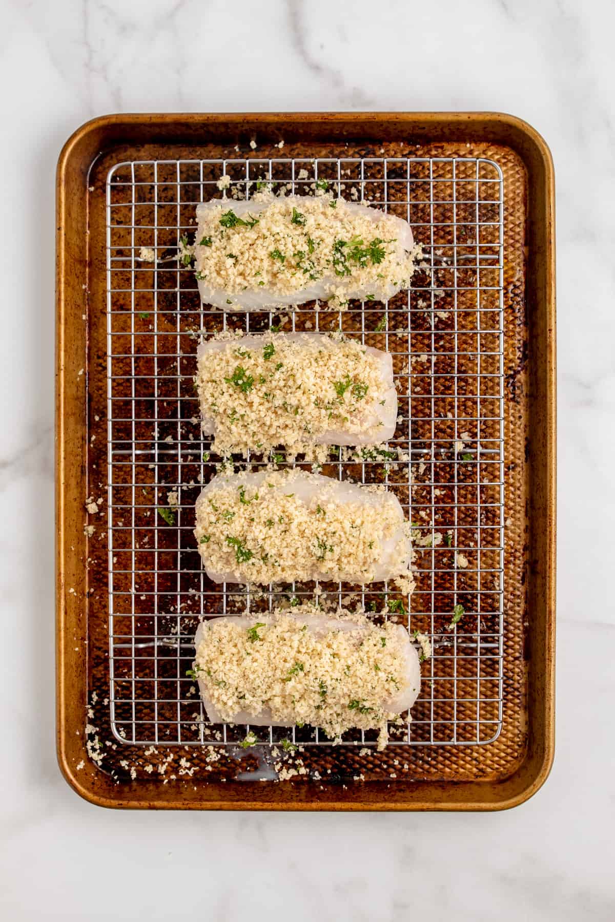 Raw cod fillets coated with panko breadcrumbs on a baking sheet.