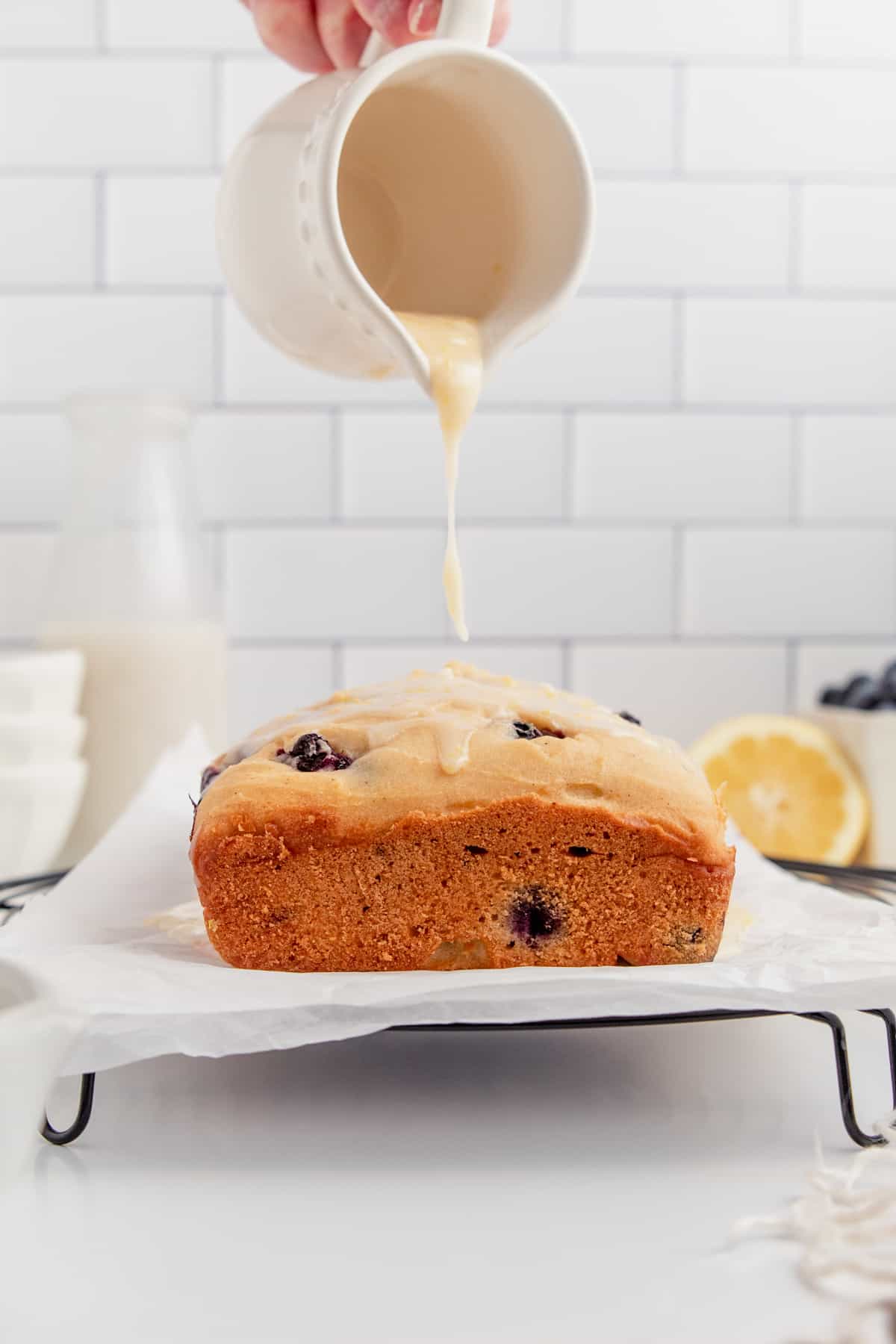 Gluten free lemon blueberry loaf being drizzled with lemon glaze.