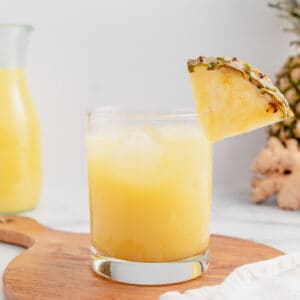 A glass of pineapple ginger juice with a pineapple wedge on it.