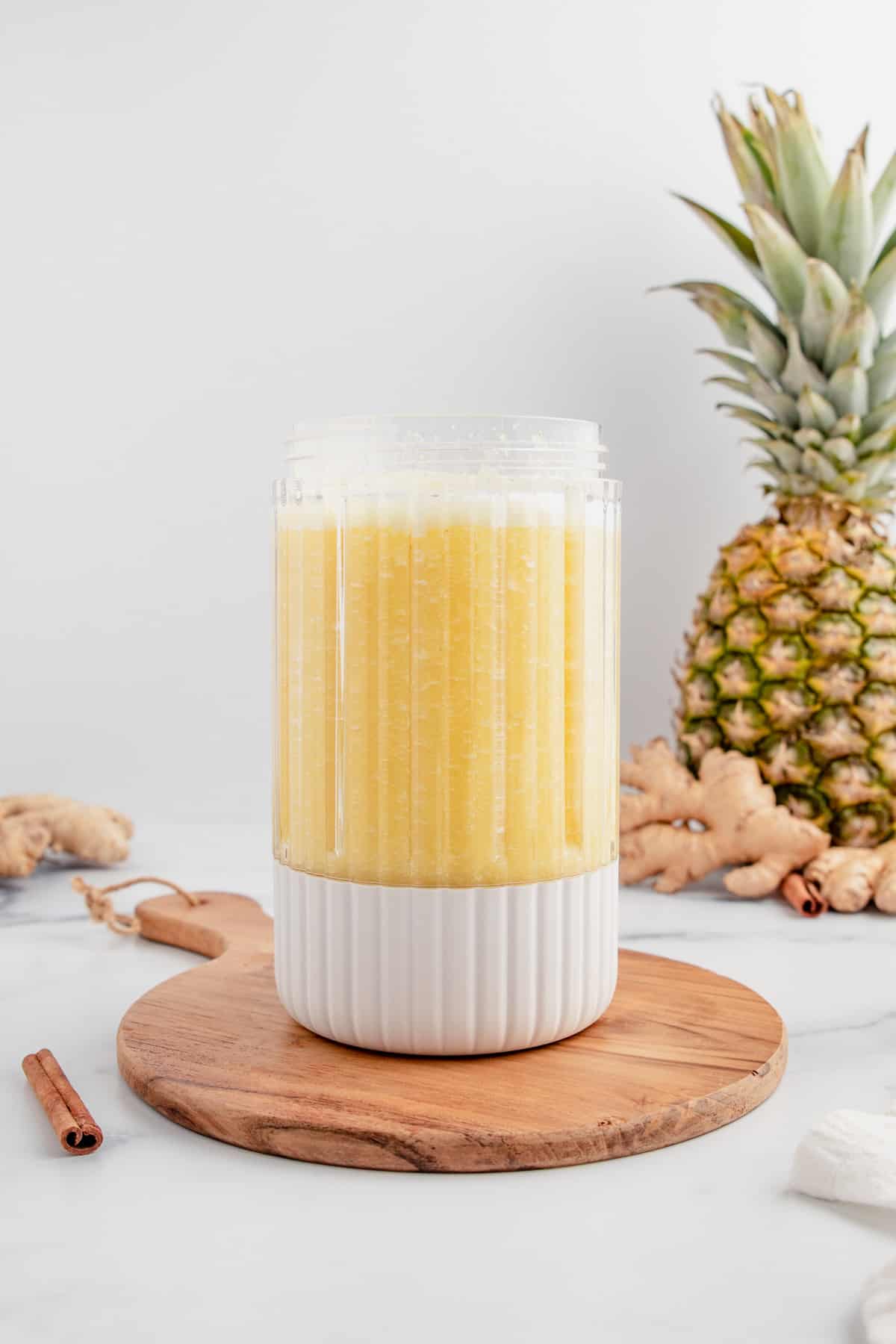 A blender full of of pineapple ginger juice with a pineapple in the background.