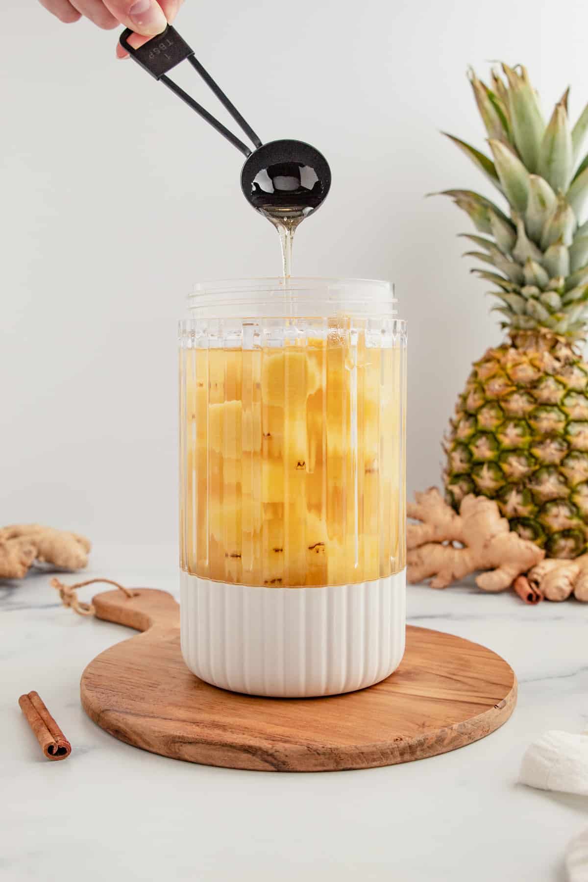 Pouring honey into a blender full of water, pineapple, and ginger.