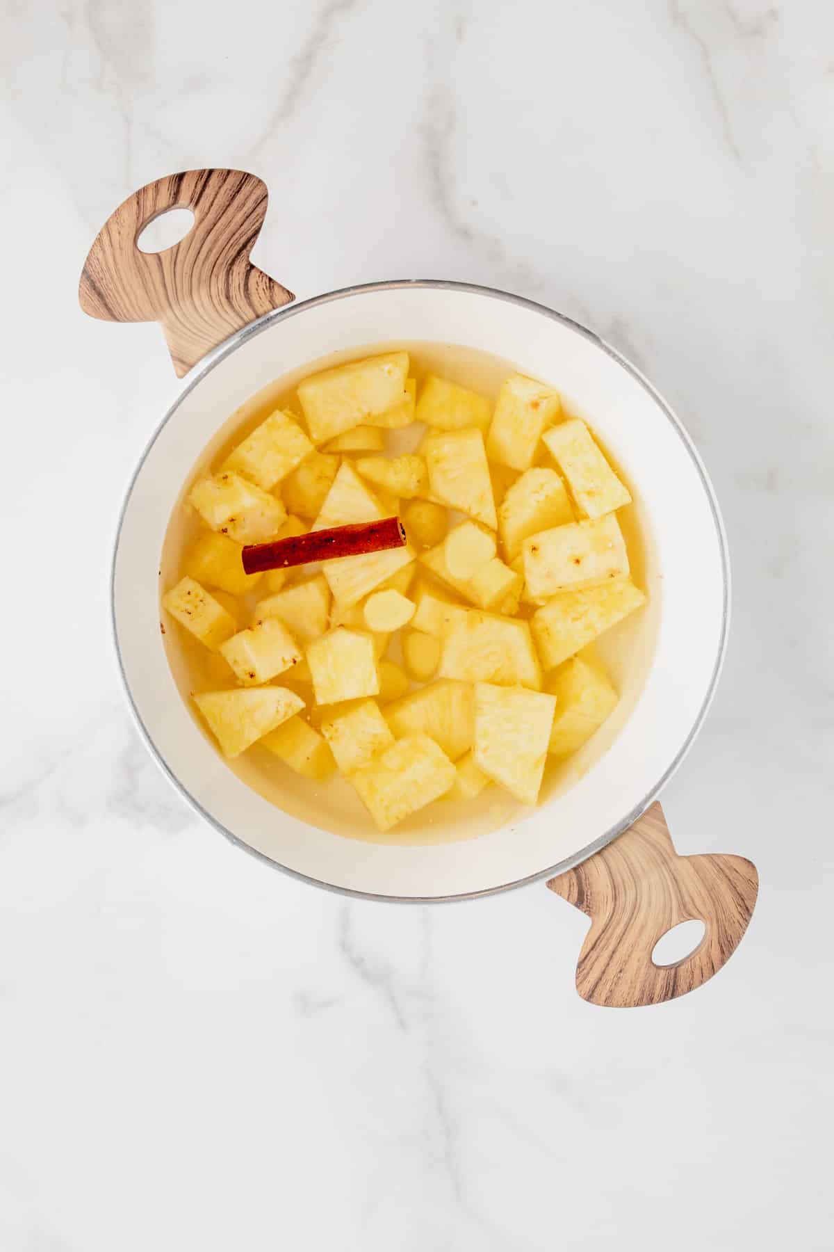 Pineapple, cinnamon, and ginger simmering in a pot full of water.