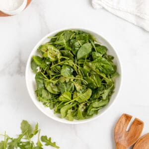 Spinach and arugula salad with balsamic vinaigrette in a white bowl.