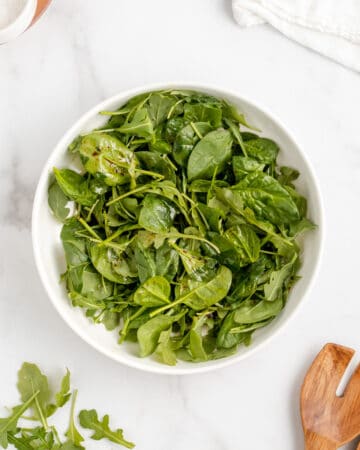 Spinach and arugula salad with balsamic vinaigrette in a white bowl.