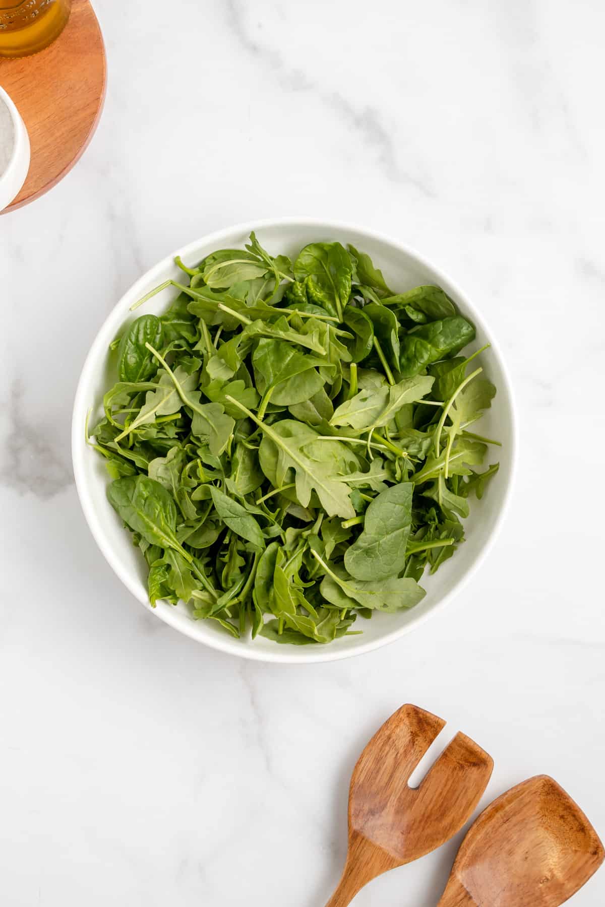 A bowl of fresh spinach and arugula with wooden tongs.