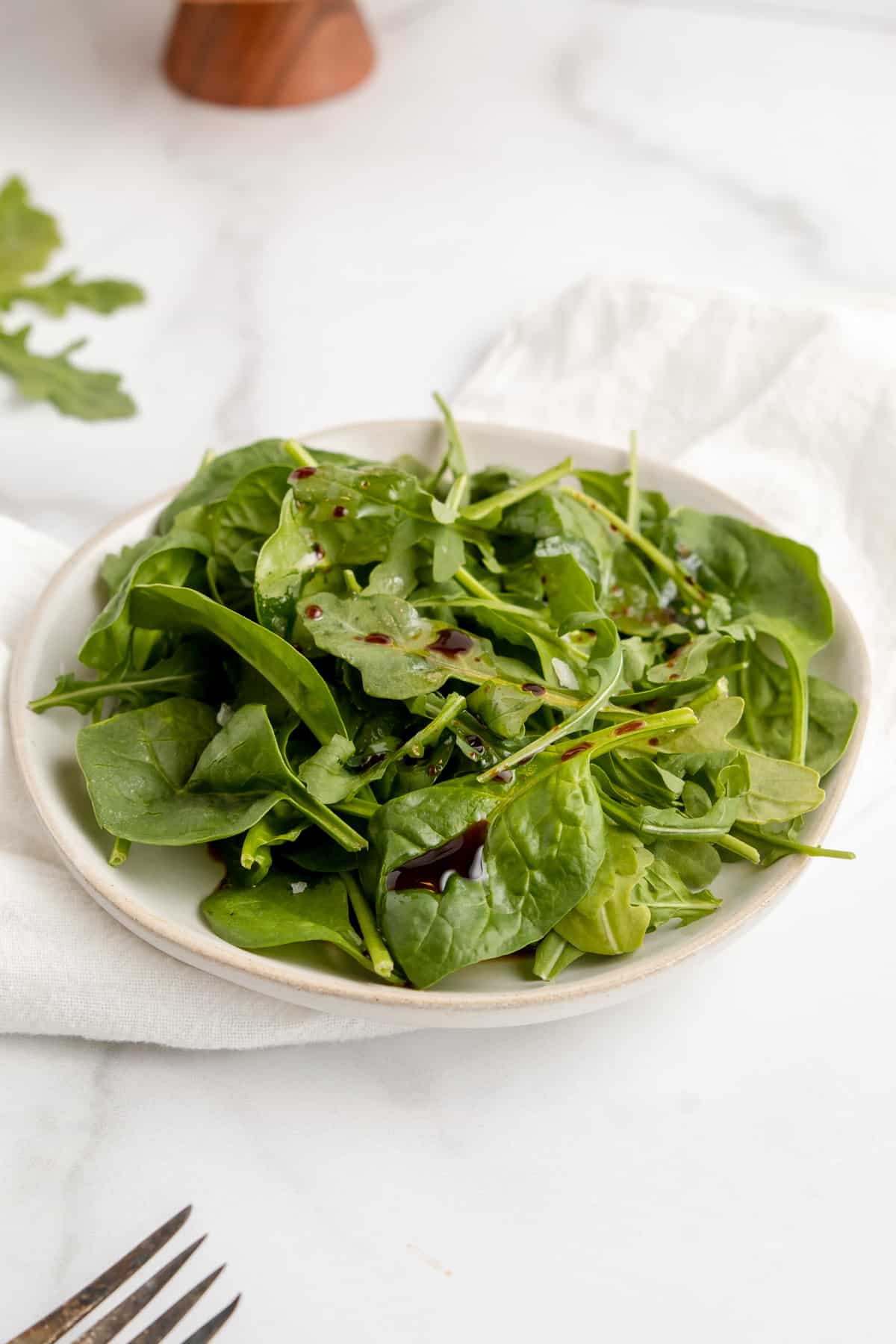 Spinach and arugula salad with balsamic vinaigrette on a white plate.