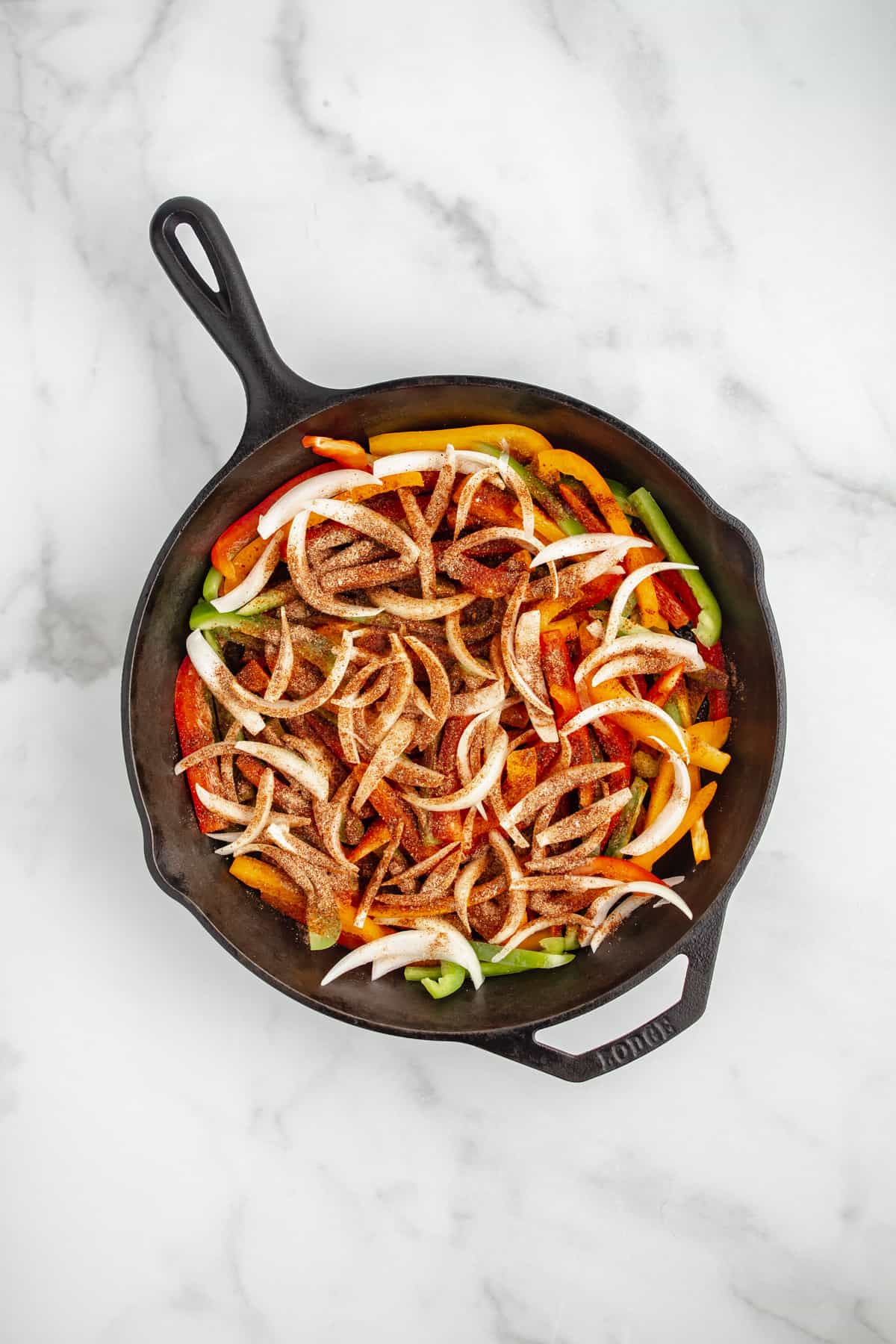 Peppers and onions in a cast iron skillet with seasonings sprinkled on top.