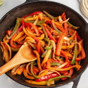 Seasoned fajita veggies in a cast iron skillet with a spoon.