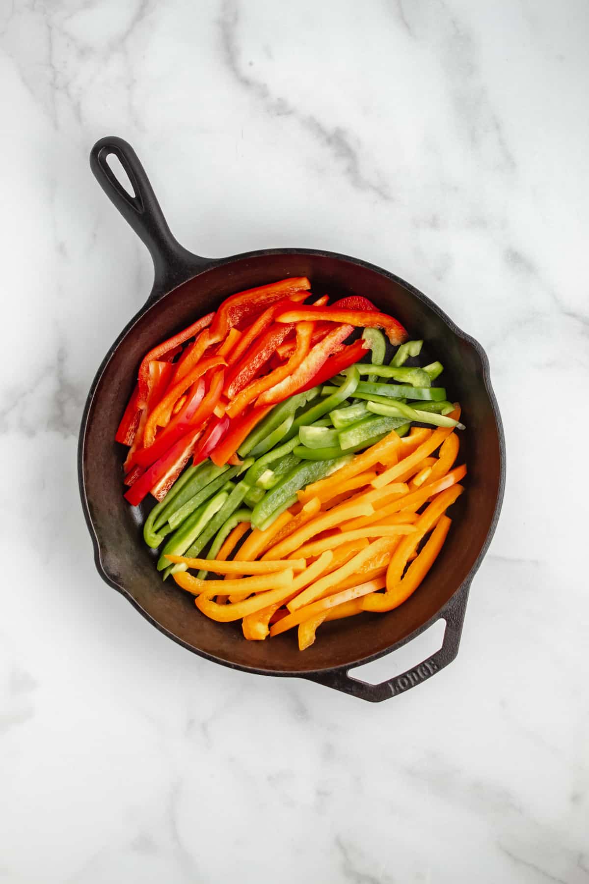 Sliced red, orange and green peppers in a cast iron skillet.