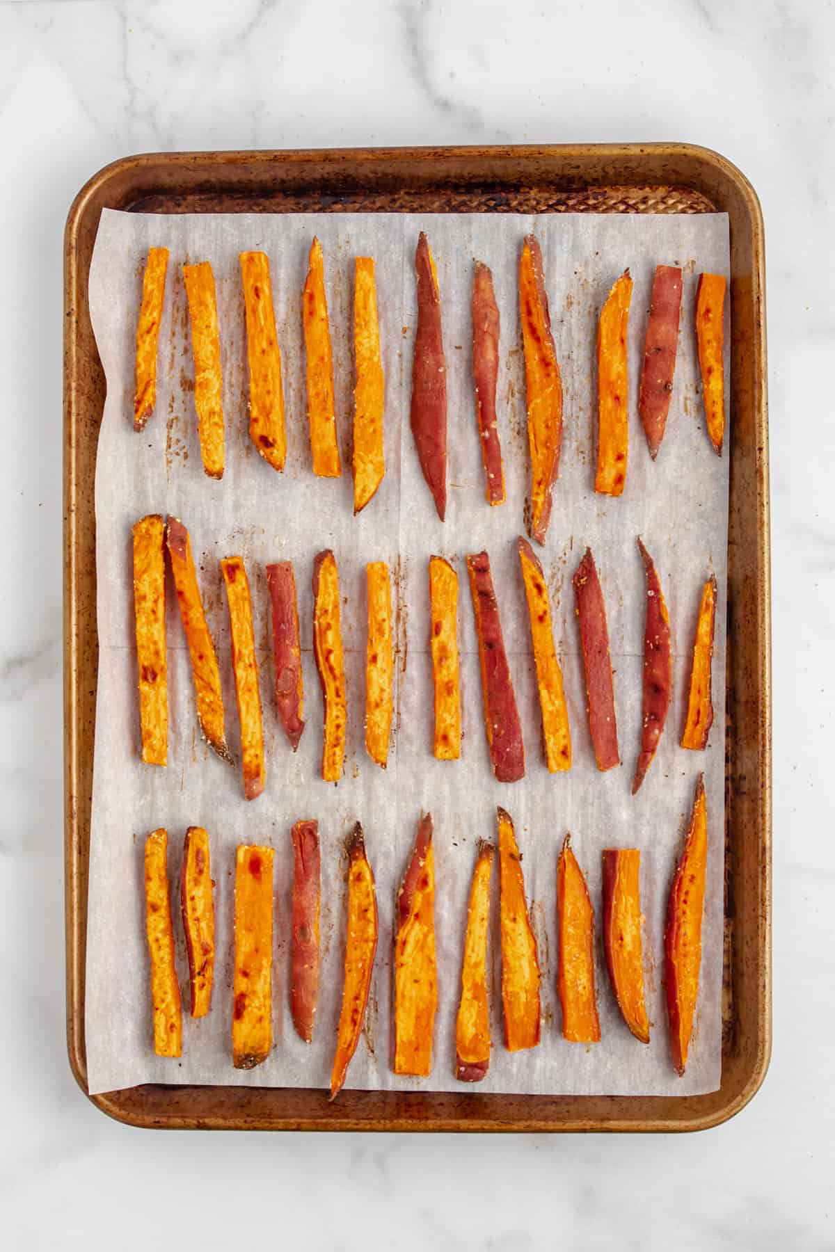 Baked sweet potato fries on a baking sheet with parchment paper.