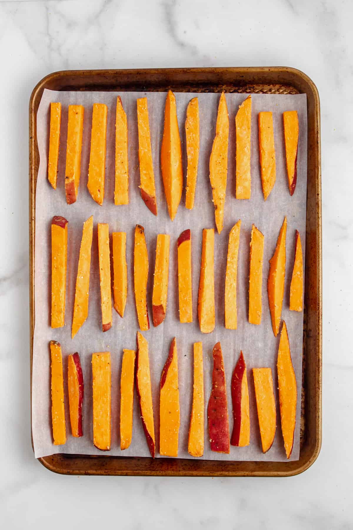 Sweet potato fries on a baking sheet with parchment paper before baking.