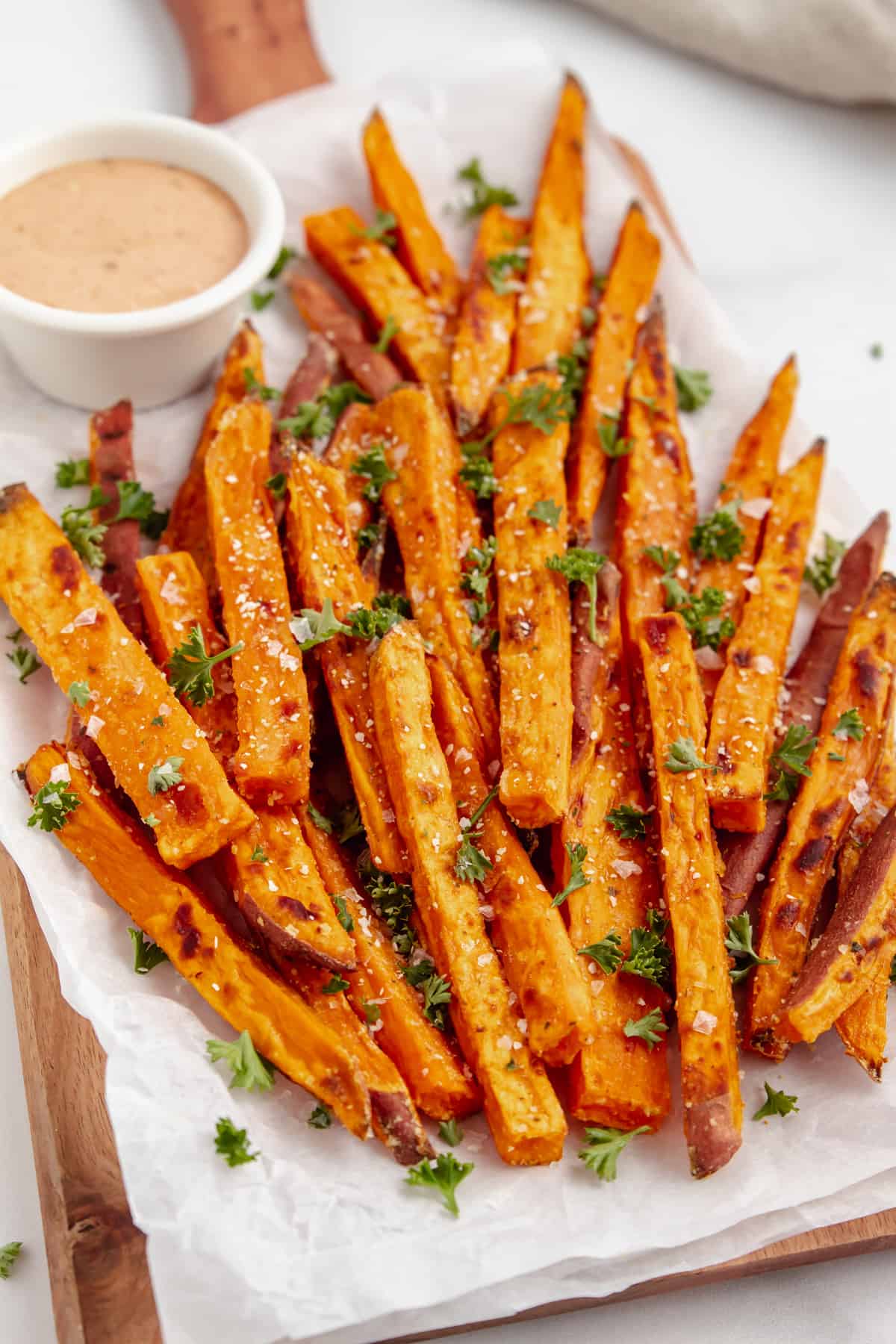 Baked sweet potato fries topped with salt and fresh herbs and a side of dipping sauce.