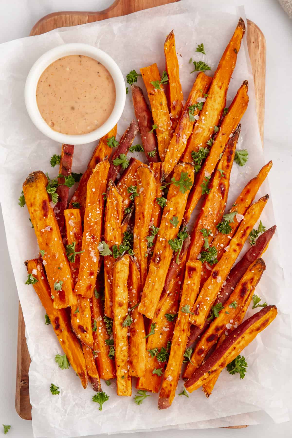 Baked sweet potato fries topped with salt and fresh herbs and a side of dipping sauce.